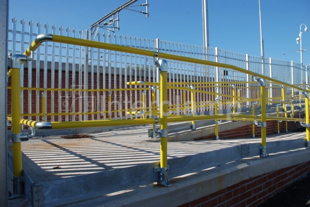 Interclamp Key Clamp DDA Assist fittings and safety yellow powder-coated handrail tube used to construct a disabled access ramp at a train station, ensuring accessibility and safety.